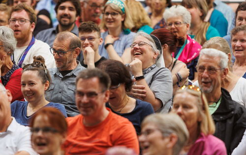 Bild eines Publikums beim Kirchentag 2023 in Nürnberg: Lachende und lächelnde Menschen verschiedenen Alters blicken in eine Richtung. Einige tragen kurzärmelige T-Shirts.