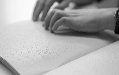 Ein Paar Hände liest Brailleschrift von einem weißen Blatt.