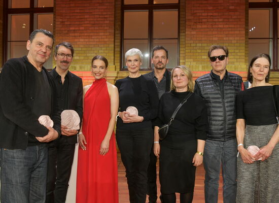 In festlicher Kleidung steht das AD-Team des Beziehungsdramas „Roter Himmel“ auf der Bühne. Es gewann die ADele in der Kategorie „Spielfilm - Kino“.  Einige Team-Mtglieder halten die Keramik-Trophäe in den Händen.