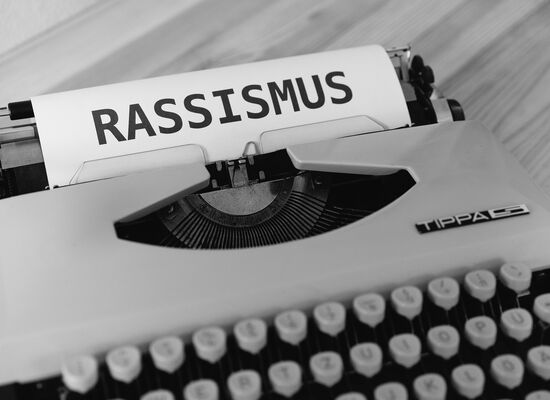 Eine Schreibmaschine mit einem angefangenen Blatt. In Großbuchstaben steht Rassismus dort geschrieben.