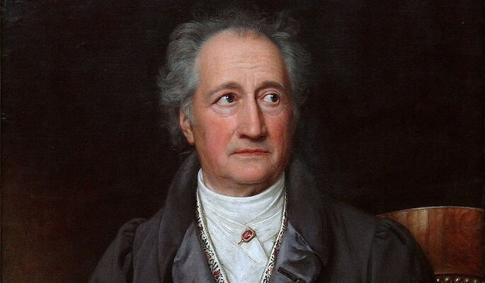 Porträt von Johann Wolfgang von Goethe, eines älteren Mannes mit grauem Haar, schwarzem Mantel und weißem Hemd. Er hält ein Schriftstück in der Hand und blickt zur Seite. Der Hintergrund ist dunkel, das Licht betont sein Gesicht.