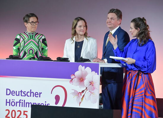 Von links nach rechts stehen Christina Marx, Christina Claussen, Andreas Bethke, Nadine Heidenreich auf der Bühne bei der Verleihung des Deutschen Hörfilmpreises. Sie sind festlich gekleidet.