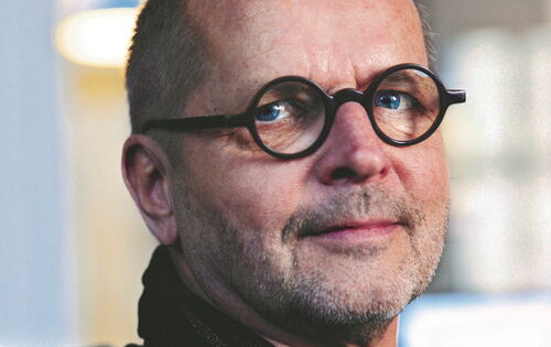 Florian Adler hat sehr kurzes Haar und einen Dreitagebart. Er trägt einen schwarzen Pullover und eine schwarze Brille mit runden Gläsern.