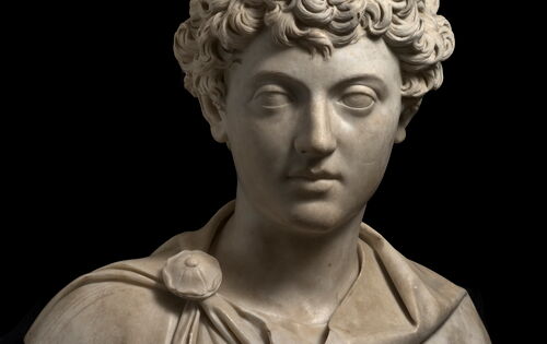 Büste von Marcus Aurelius, die den jungen Mann mit lockigen Haaren und vollen Lippen zeigt. An seiner Schulter befästigt eine runde Brosche seinen Umhang.