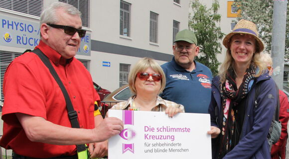 Auf einem Gehweg: Bodo Rinas (links) und Margrit Richter (2.v.l.) übergeben die plakatgroße Urkunde zur schlimmsten Kreuzung an die Behindertenbeauftragte von Königs Wusterhausen, Friederike Weigelt (mittig). Weitere Beteiligte schauen zu.
