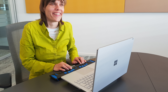 Franziska Sgoff trägt ihr glattes Haar schulterlang. Sie sitzt lächelnd an einem aufgeklappten Laptop.