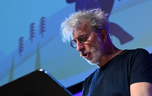 Rufus Beck ließt "Bummel durch Europa" von Mark Twain. Er trägt ein dunkles T-Shirt und eine runde Brille. Sein dichtes Haar und sein Bart sind grau.