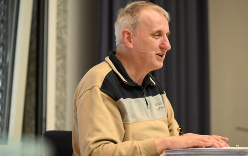 Christian Spremberg halb von der Seite fotografiert. Er liest einen Text in Brailleschrift vor. Er hat graues Haar und trägt ein Sweatshirt.