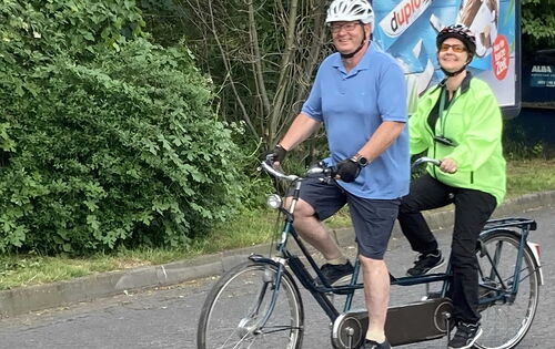 Petra Bognitz und ihr Pilot Volker Weinlich fahren auf einem Tandem eine Straße entlang. Beide tragen einen Helm.