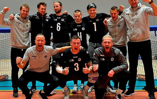 Das Goalball-Team Deutschland steht jubelnd vor dem Tor. Es sind zehn weiße Männer in Sportkleidung. Sie haben einander die Arme über die Schulter gelegt