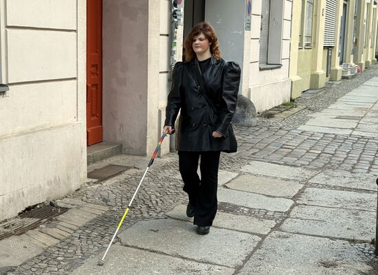 Marie Lampe geht mit ihrem Langstock pendelnd eine Straße entlang.
