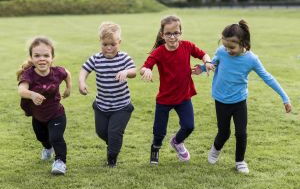 Vier Kinder, zum Teil mit Behinderung, rennen Hand in Hand über eine Wiese. Sie tragen bunte T-Shirts und haben Spaß.