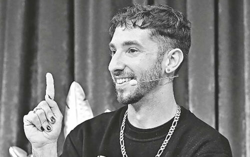 Noam Brusilovsky hebt lachend den linken Zeigefinger. Seine Nägel sind lackiert. Er trägt einen schwarzen Pullover mit dem Aufdruck "Kein Mensch ist illegal".