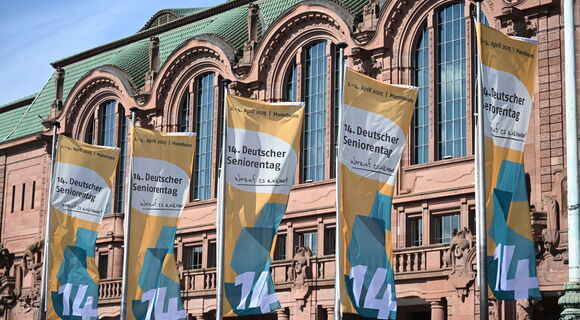 Mehrere Fahnen mit der Aufschrift „14. Deutscher Seniorentag – Worauf es ankommt“ wehen vor der Fassade des Congress Centers Rosengarten in Mannheim. Die Veranstaltung fand vom 2. bis 4. April 2025 statt.