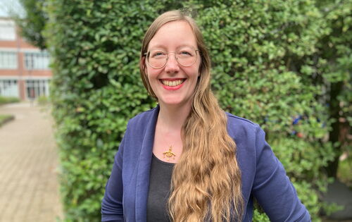 Julia Witte hat lange hellere Haare, eine große Brille mit schmalem Rand und schaut lachend in die Kamera. Sie trägt ein dunkles Oberteil, darüber einen Blazer sowie eine Halskette mit einem großen Anhänger.