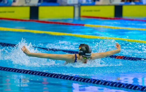 Die 14-jährige Johanna Döhler schwimmt in Schmetterlingstechnik, auch Delfin genannt, eine Bahn: Sie hat die Arme zur Seite ausgebreitet und holt Luft. Sie trägt eine dunkle Badekappe und eine Schwimmbrille.