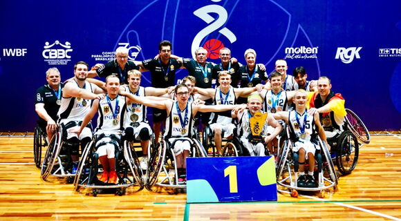 Gruppenfoto des Para-Teams 2025 der U23 Rollstuhlbasketballmannschaft. Die Männer haben die Arme ausgebreitet, ihre Hände liegen jeweils auf den Schultern der Teamkollegen neben ihnen.