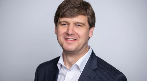 Thomas Krämer hat kurzes dichtes dunkleres Haar. Er trägt ein dunkles Sakko und ein weißes Hemd. Sein Blick ist freundlich lächelnd zur Kamera gerichtet.