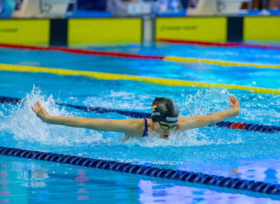 Die 14-jährige Johanna Döhler schwimmt in Schmetterlingstechnik, auch Delfin genannt, eine Bahn: Sie hat die Arme zur Seite ausgebreitet und holt Luft. Sie trägt eine dunkle Badekappe und eine Schwimmbrille.