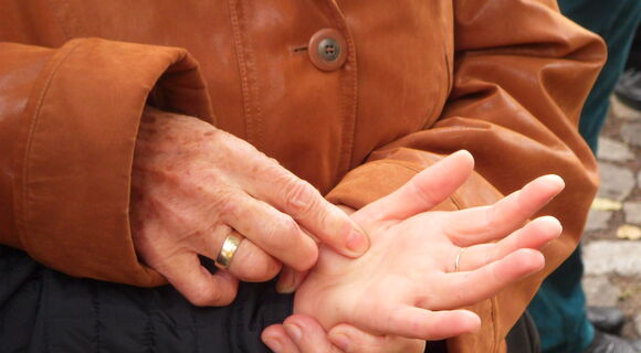 Nahaufnahme von sich berührenden Händen beim Lormen: Die linke Hand einer Person liegt mit der Handfläche nach oben in der linken Hand einer zweiten Person. Diese tippt mit den Fingern ihrer rechten Hand Lormzeichen in die Hand der ersten Person.
