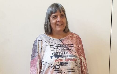 Heike Kühner steht vor einer Wand. Sie hat glattes, nackenlanges, helles Haar und einen Pony. Ihr T-Shirt ist hell, ihre Hose dunkel.