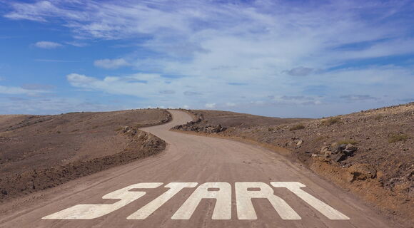 "Start" steht in großen Lettern auf einer Straße, die gewunden zum Horizont führt.