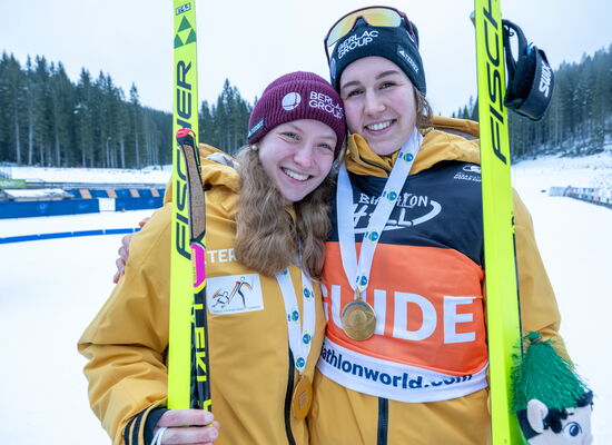 Mit Skiausrüstung, Skiern in den Händen und Medaillen um den Hals stehten die Para-Sportlerin 2025, Johanna Recktenwald (links) und ihr Guide Emily Weiss nebeneinander in einer verschneiten Landschaft.