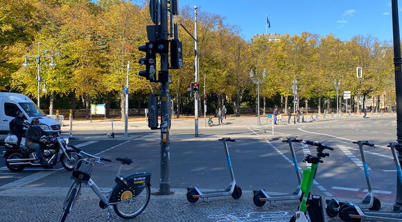 Auf einem Gehweg stehen kreuz und quer verschiedenfarbige E-Roller.