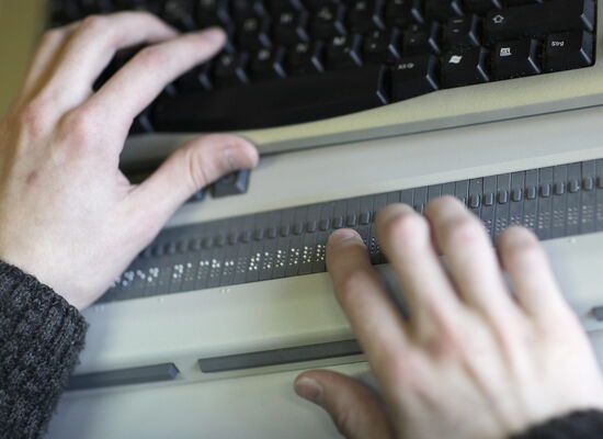 Ein Paar Hände liest auf einer Braillezeile an einem Laptop.
