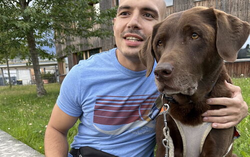 Nikolaos Rizidis hat eine Glatze und einen Schnurrbart. An seiner Seite sitzt sein Blindenführhund Orlando, ein Labrador-Retriever.