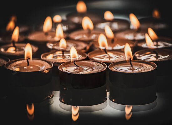 Viele Teelichter stehen auf einer spiegelnden Oberfläche. Das Licht der Flammen der vorderen drei Lichter spiegelt sich darin.