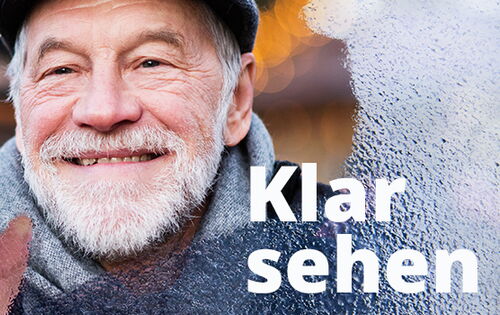 Ein älterer Mann mit grauem Bart und Mütze blickt lächelnd durch eine beschlagene Glasscheibe. Die rechte Hand wischt das Glas frei. Rechts unten steht in weißer Schrift „Klar sehen“.