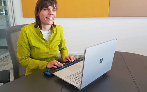 Franziska Sgoff trägt ihr glattes Haar schulterlang. Sie sitzt lächelnd an einem aufgeklappten Laptop.